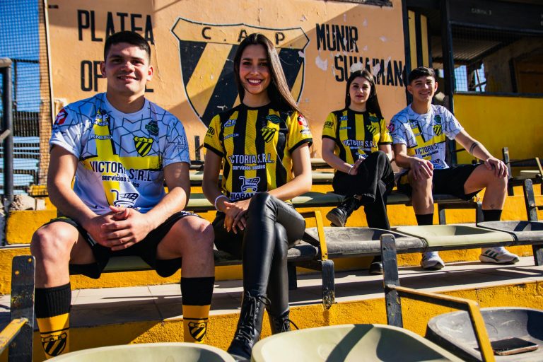 Four soccer fans in team jerseys sitting in a stadium, enjoying the game atmosphere.